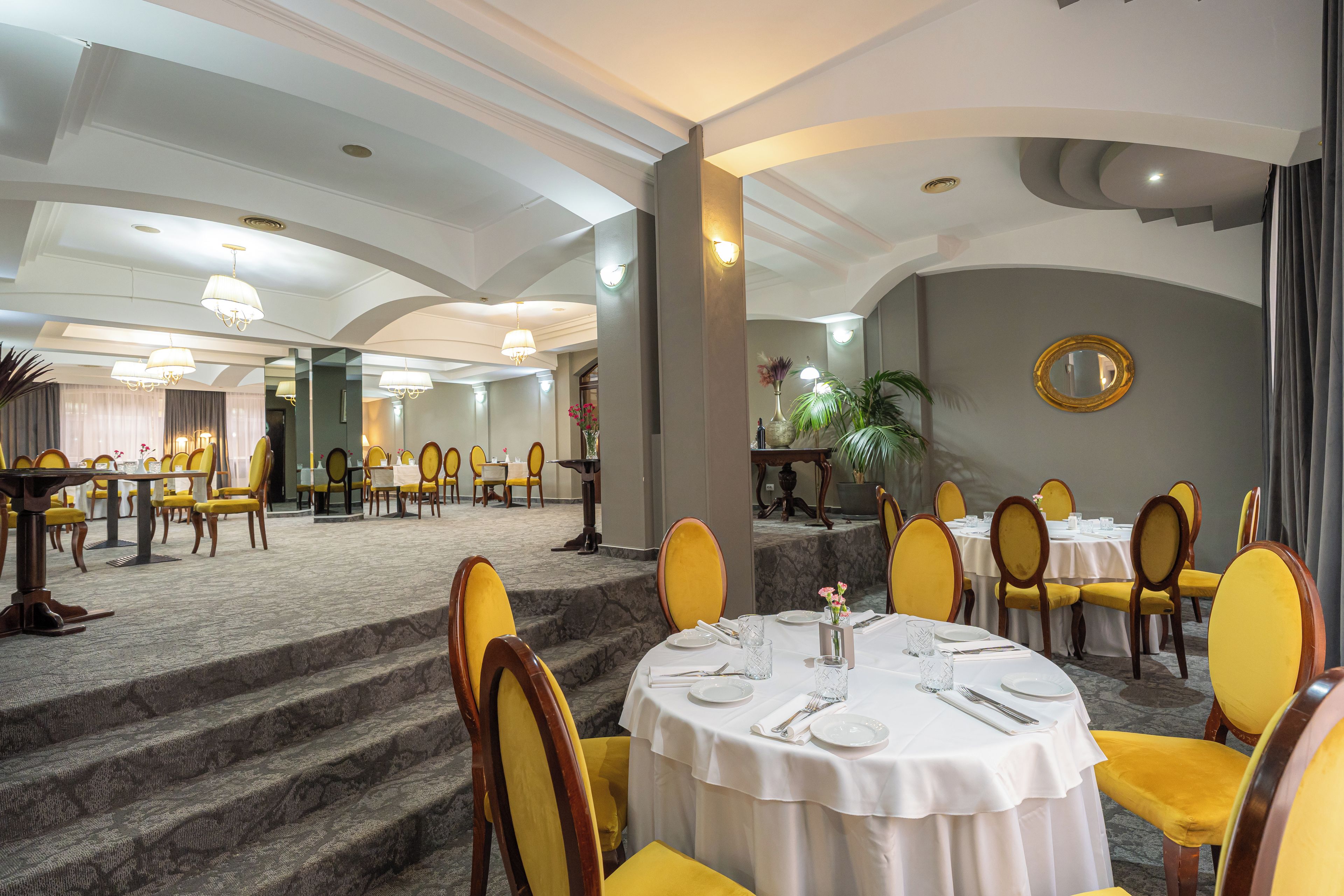 A hotel dining area with round tables, yellow chairs, and a marble staircase.