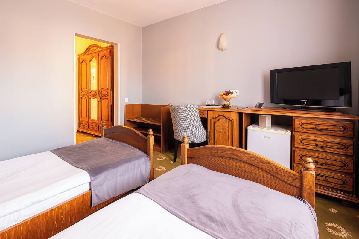 Una habitación de hotel con dos camas individuales, un escritorio de madera con televisor, un refrigerador pequeño y un armario.