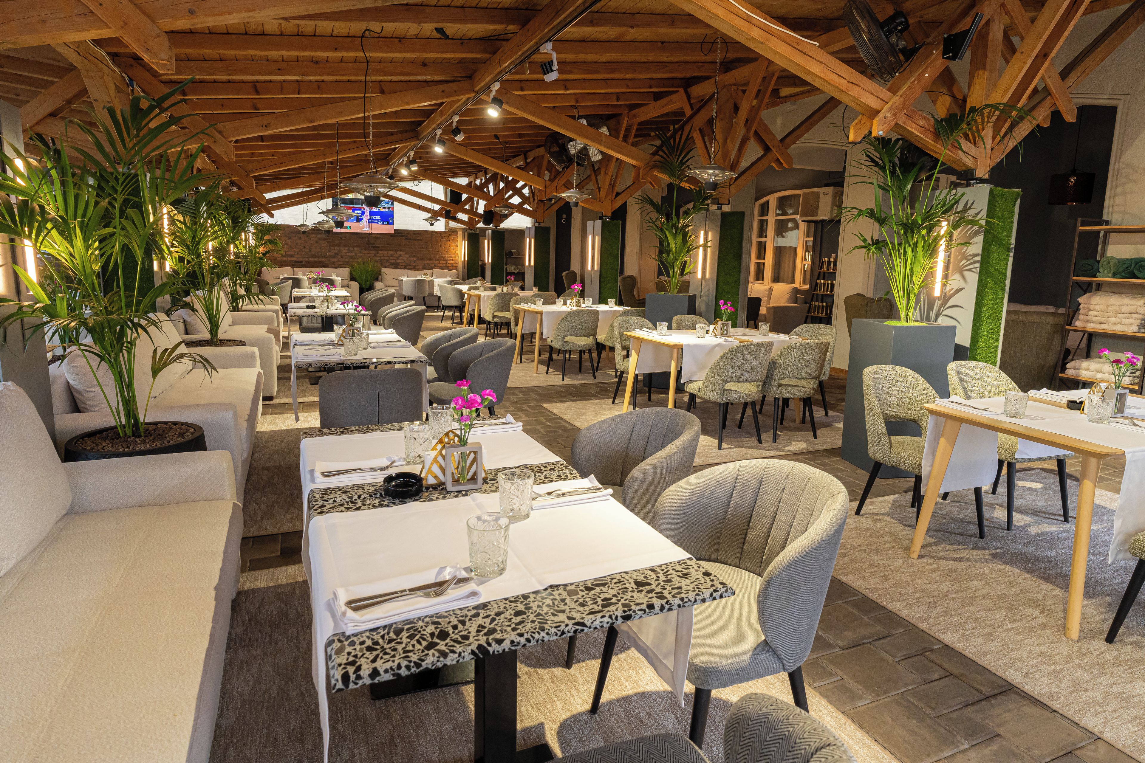 A restaurant with wooden beams, tables with white tablecloths, and chairs.