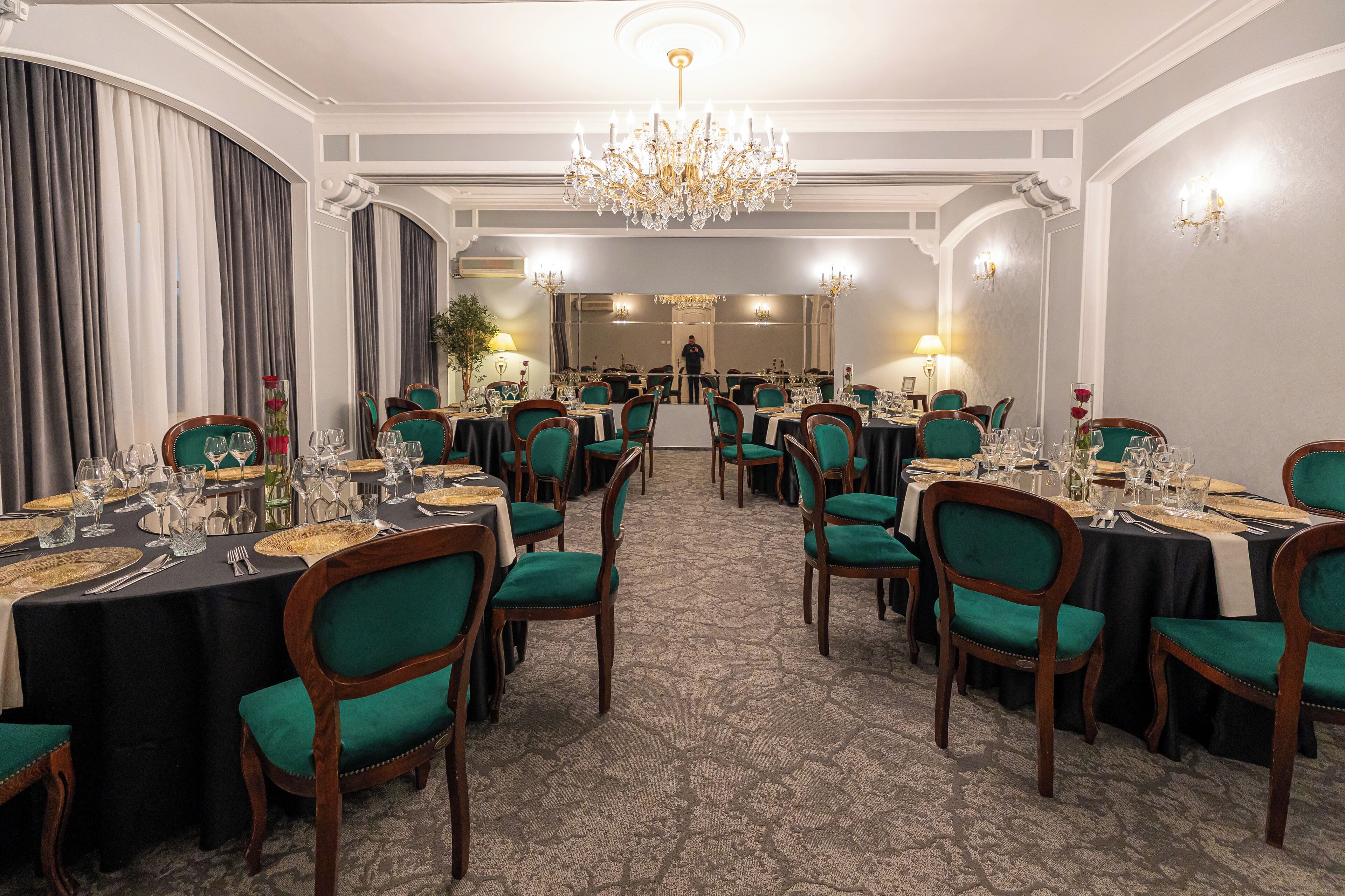 A formal dining room with multiple tables set for service, a chandelier, and a person in the background.
