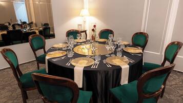 Mesa redonda para comer con mantel negro, rodeada de sillas tapizadas en verde.