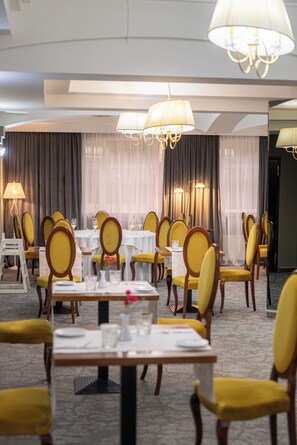 Ein Hotelrestaurant mit gedeckten Tischen, gelben Sitzmöbeln und Kristalllüstern.