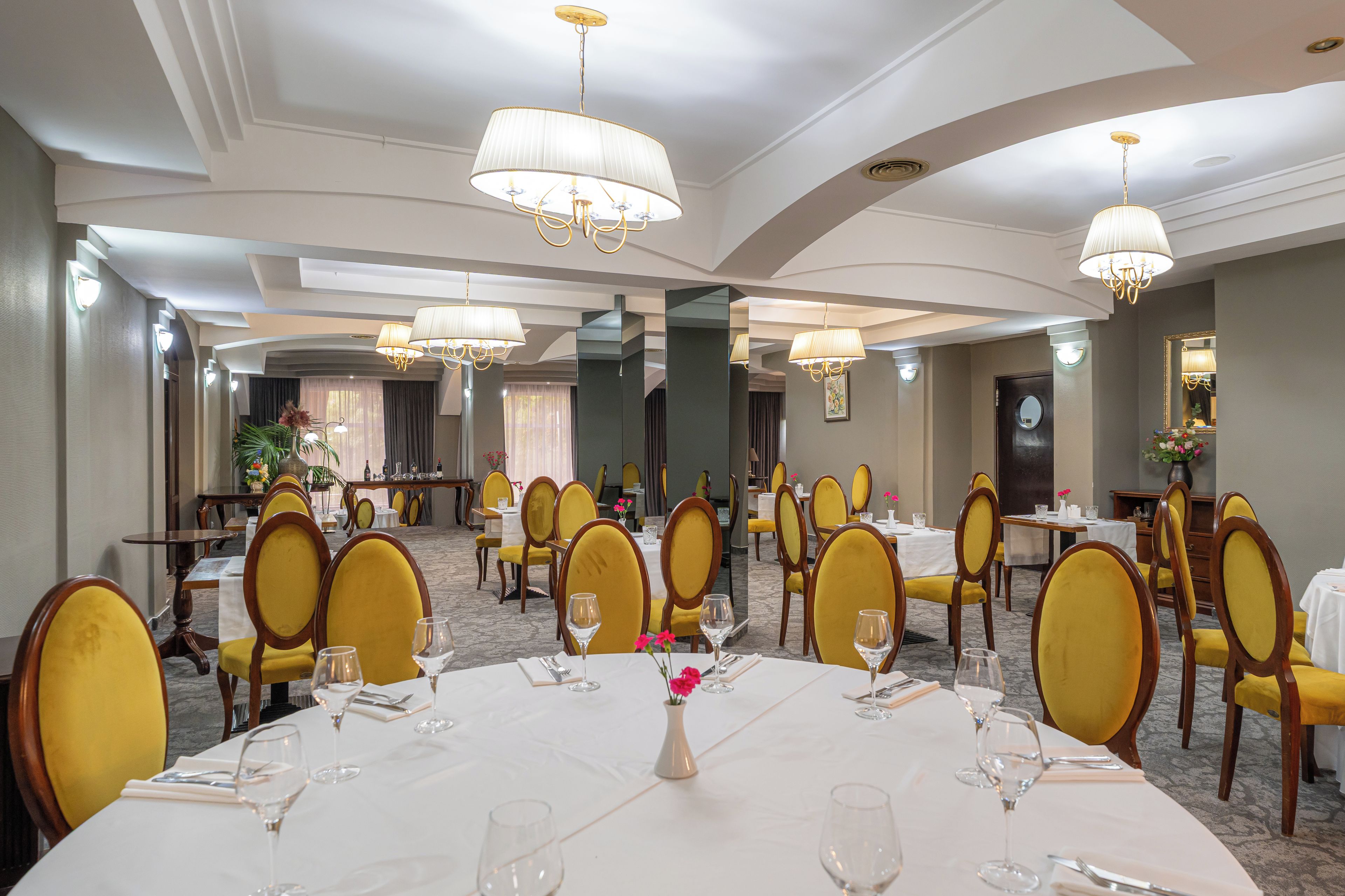 A hotel dining area with round tables, yellow chairs, and chandeliers.