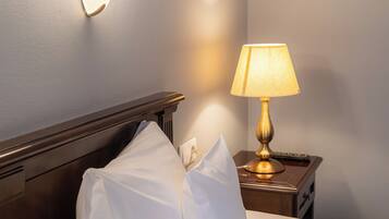 A neatly made bed with white linens and pillows, a bedside lamp, and a wall-mounted light fixture.