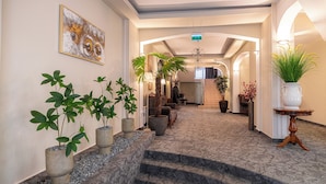 A hotel lobby with a marble staircase, potted plants, and a large painting on the wall.
