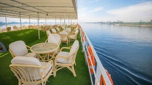 A deck with wicker chairs and tables, overlooking a calm body of water. - Nile Cruise Majesty every Monday from Aswan 3 nights and every Thursday from Luxor 4 nights (Aswan)
