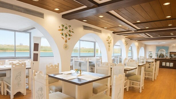 A dining area with white chairs and tables, wooden floors, and large windows offering a view of the sea. - Nile Cruise Majesty every Monday from Aswan 3 nights and every Thursday from Luxor 4 nights (Aswan)