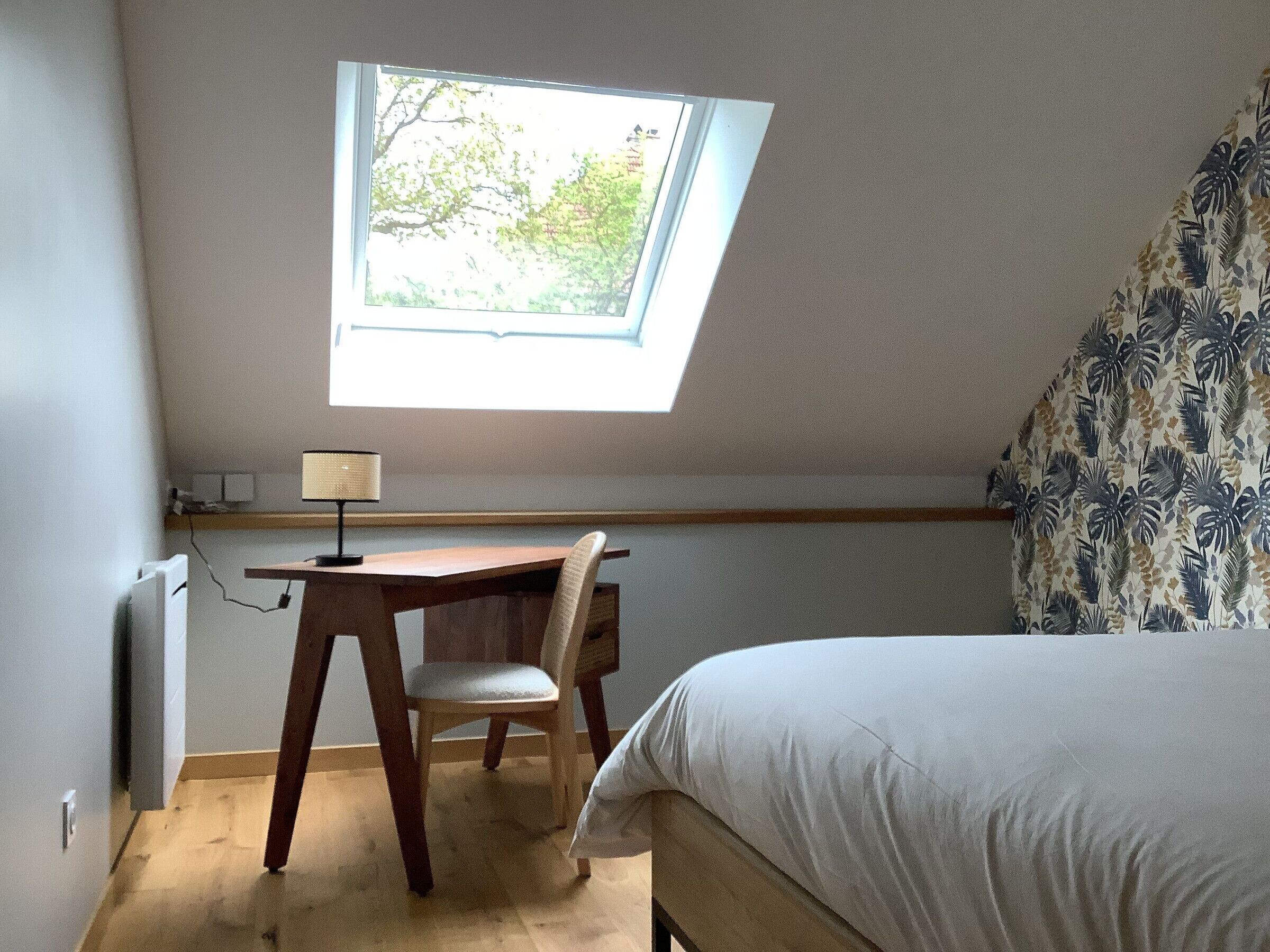 A bedroom with a skylight, a desk, a chair, and a bed.