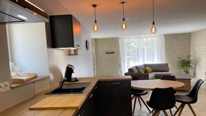 Una cocina moderna con una isla central, un comedor con una mesa redonda y sillas, y una sala de estar con un sofá y una planta.