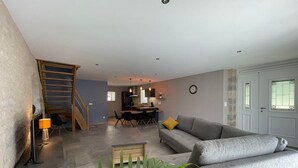 Una sala moderna con un sofá gris, una escalera de madera y un comedor con una mesa y sillas de madera.