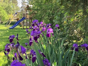 A garden with purple flowers, a wooden play structure, and a slide.
