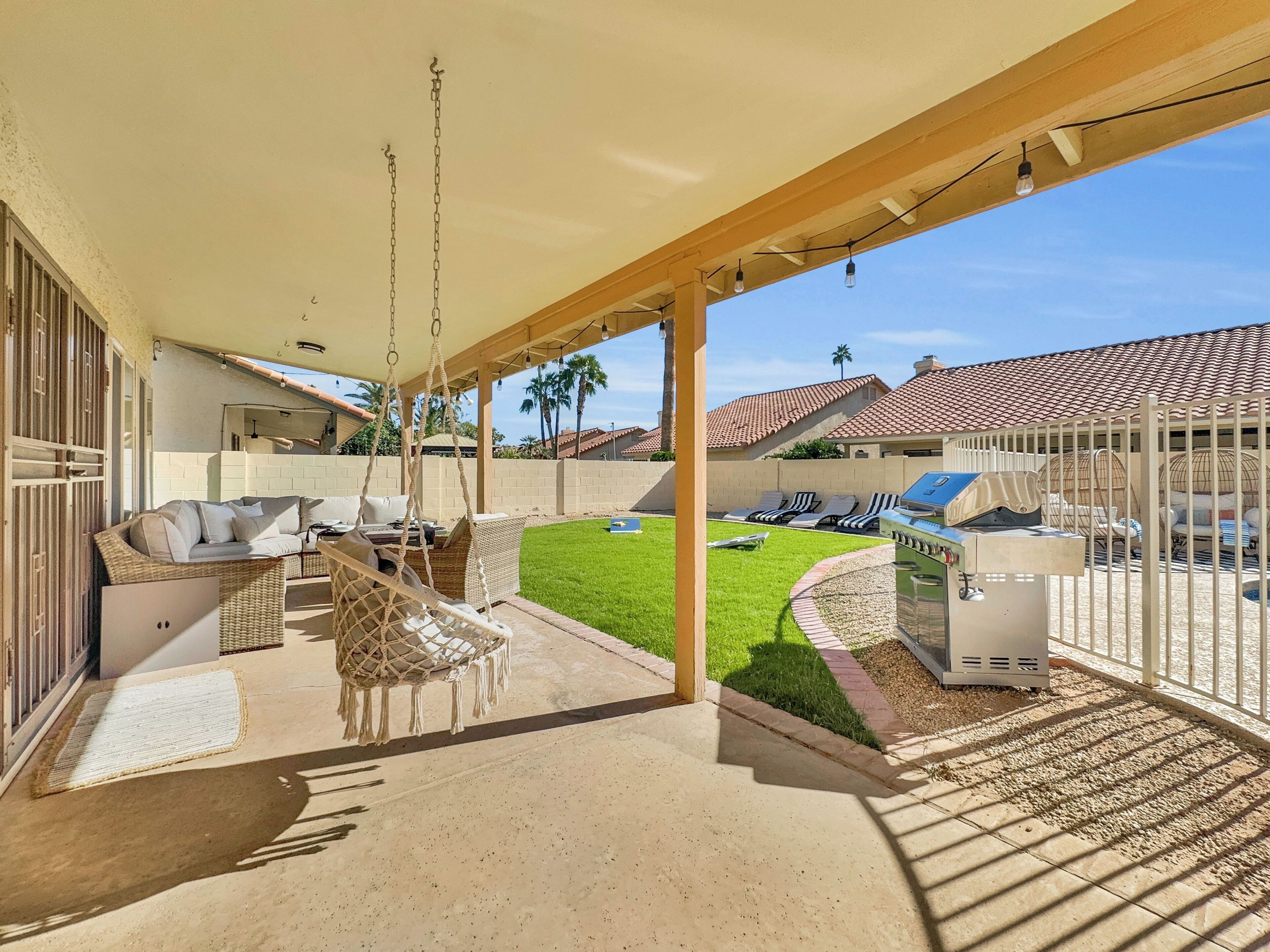 A covered patio area with outdoor seating, a grill, and a view of the neighborhood.