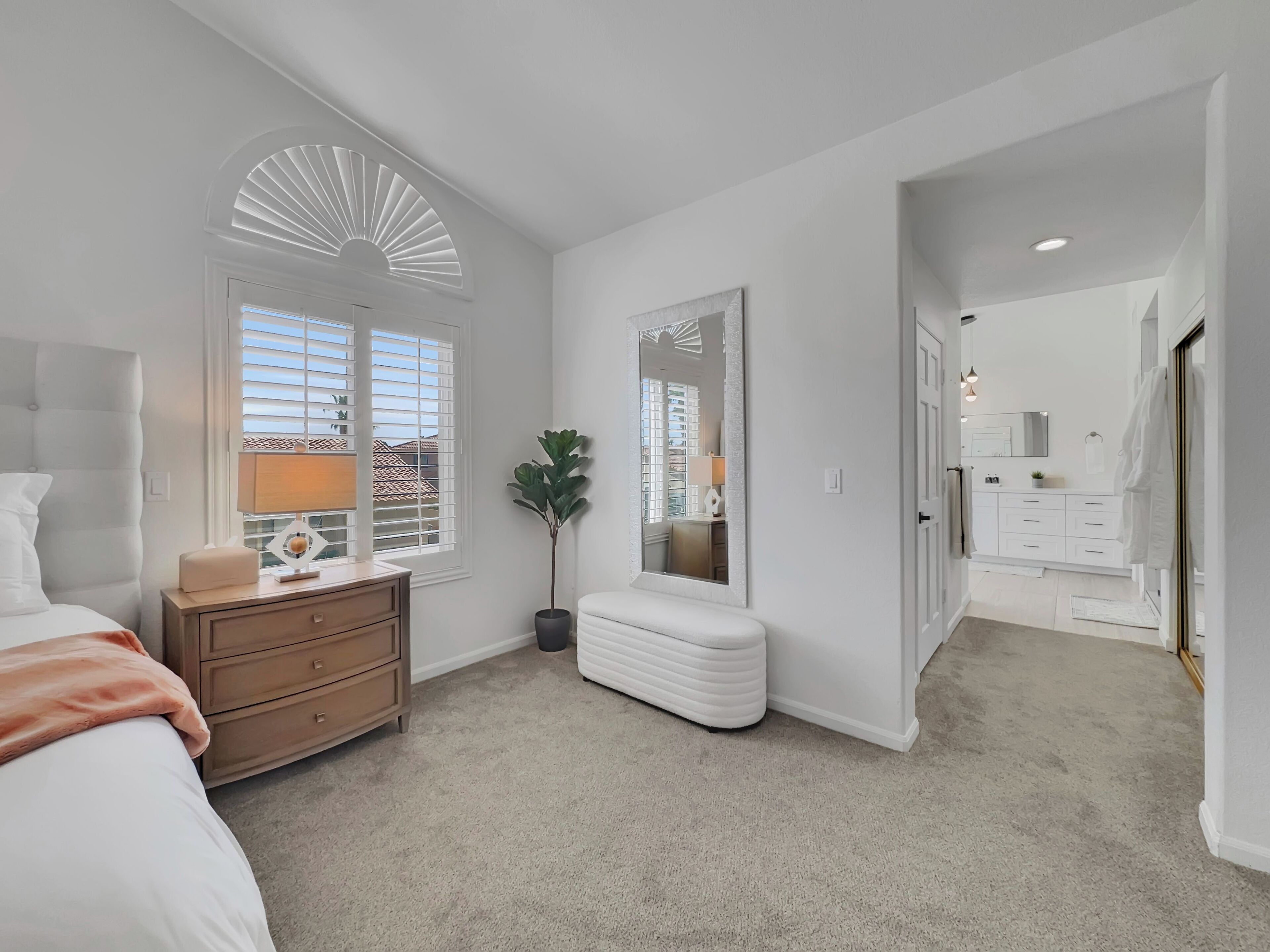 A bedroom with a bed, dresser, vanity, and a large mirror.