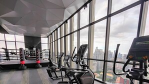 Un gimnasio con equipamiento de ejercicio, amplias ventanas y vista a la ciudad.
