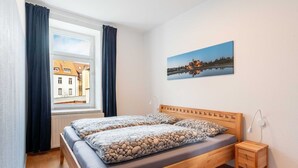 Ein Schlafzimmer mit einem hölzernen Bett, einem Nachttisch, einem Fenster mit Vorhängen und einem Stadtbild an der Wand.