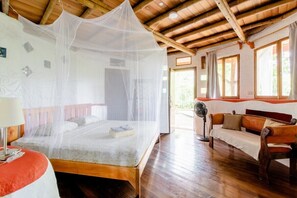 A room with a bed under a mosquito net, a wooden ceiling, a sofa, and a window. - Paradiselodge - Poolvilla - next to Nauyaca (Platanillo de Baru)