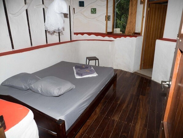 A single bed with grey bedding and pillows, a small bedside table, and a wooden floor.