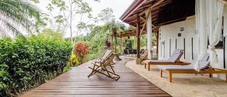 A wooden deck with lounge chairs and a covered area with white curtains.