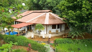 A house with a sloped roof, a swimming pool, and a wooden deck with outdoor furniture. - Paradiselodge - Poolvilla - next to Nauyaca (Platanillo de Baru)