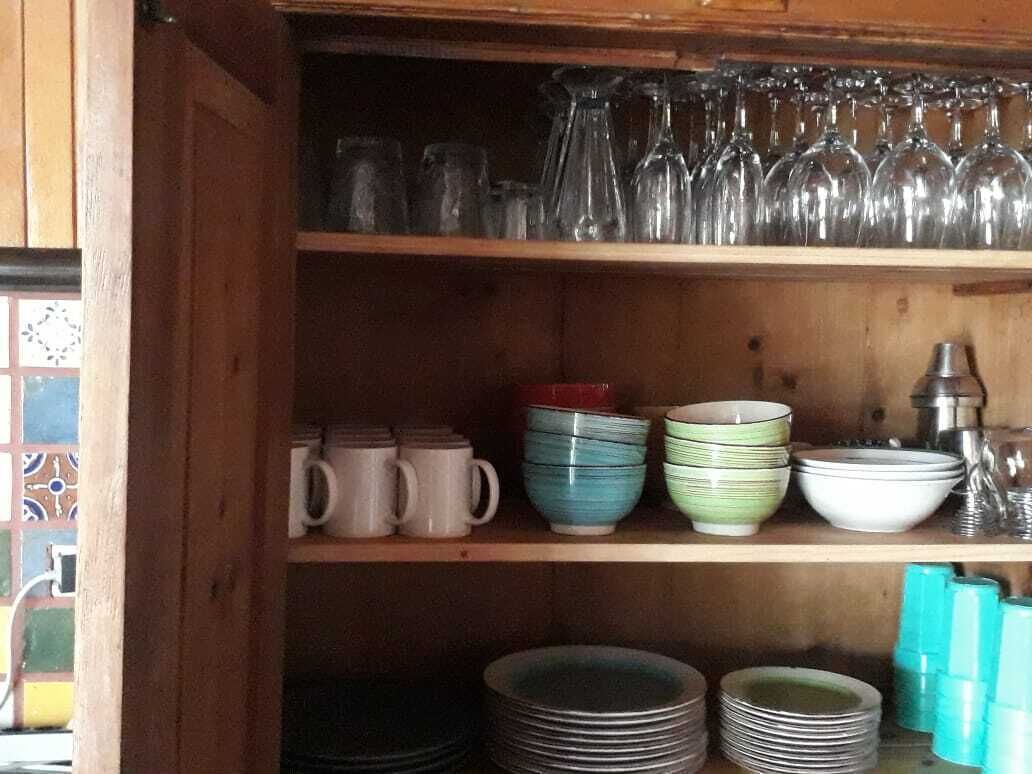 A wooden shelf with various glassware, mugs, and plates.