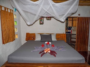 A bed with a grey bedspread, a decorative floral arrangement, and a mosquito net above. - Paradiselodge - Poolvilla - next to Nauyaca (Platanillo de Baru)