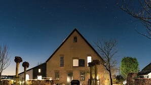 A large, triangular brick building with a car parked in front, surrounded by trees and a starry night sky. - Rural Private Loft (Meerkerk)