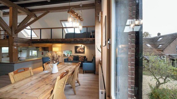 A spacious loft-style room with a wooden dining table, wicker chairs, and a large window overlooking a garden. - Rural Private Loft (Meerkerk)
