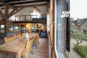 A spacious loft-style room with a wooden dining table, wicker chairs, and a large window overlooking a garden. - Rural Private Loft (Meerkerk)