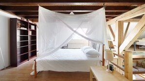 A bedroom with a canopy bed, wooden beams, a bookshelf, and a desk with a lamp. - Rural Private Loft (Meerkerk)