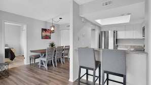 A modern kitchen with stainless steel appliances, a dining area with a wooden table and chairs, and a visible skylight.