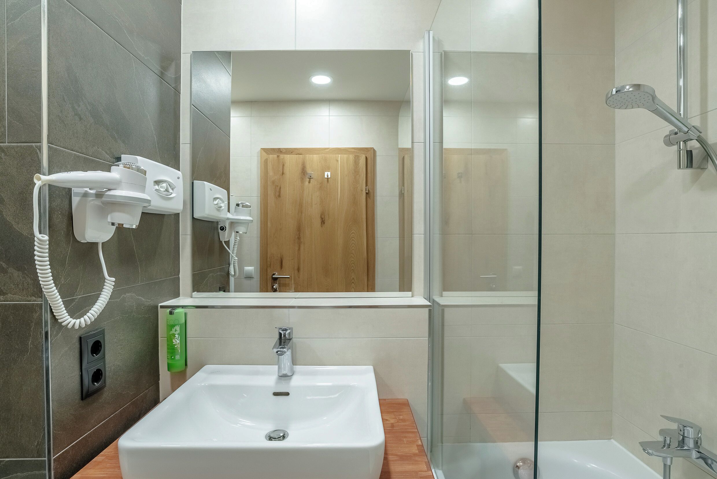 Un baño con un lavabo blanco, un box de ducha de cristal y una puerta de madera al fondo.