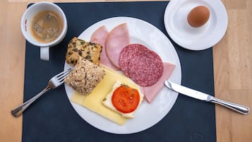 Un plato con jamón, salami, queso, tomate y pan, una taza de café y un cuchillo sobre una mesa.
