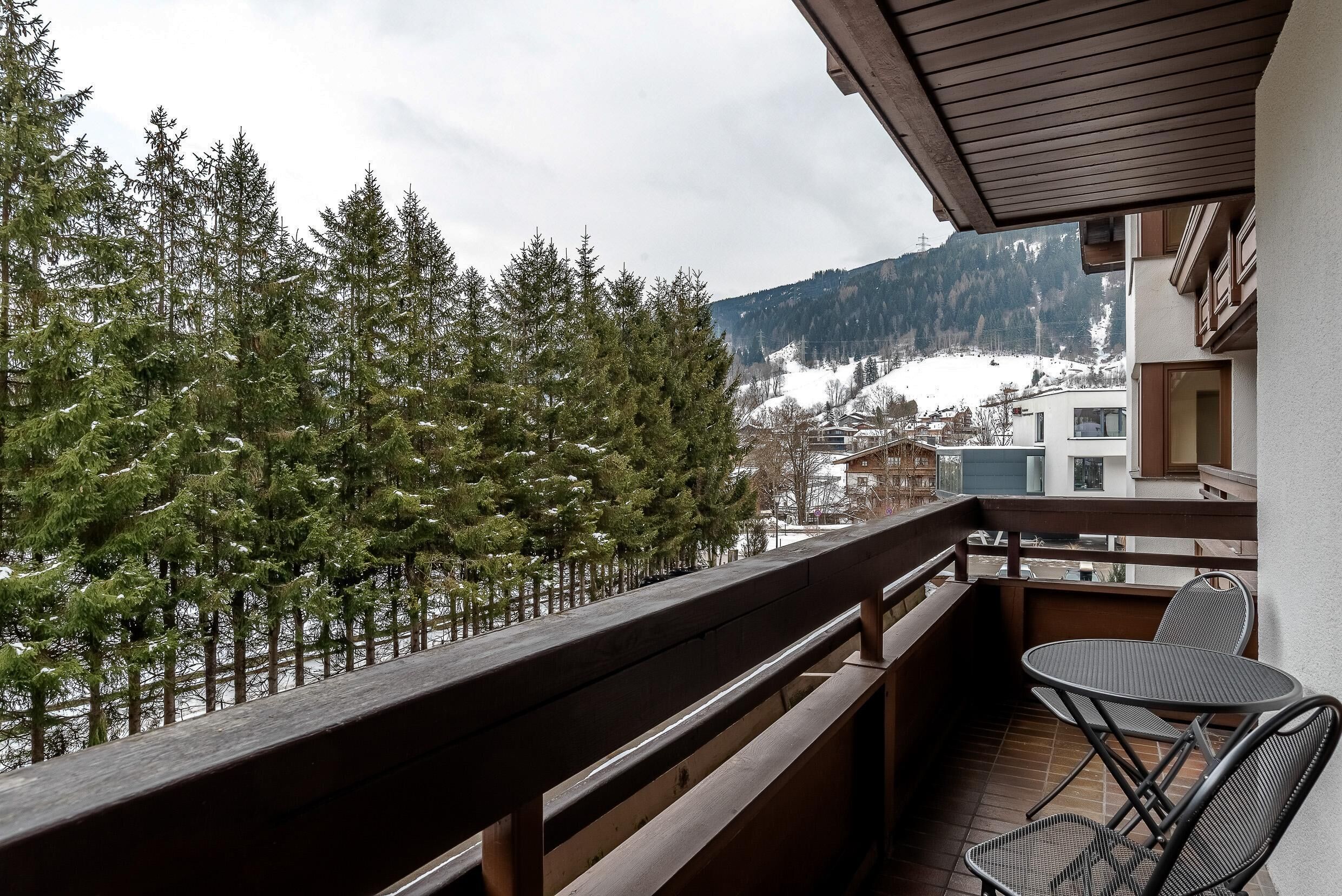 A balcony with a view of snow-covered mountains and pine trees.
