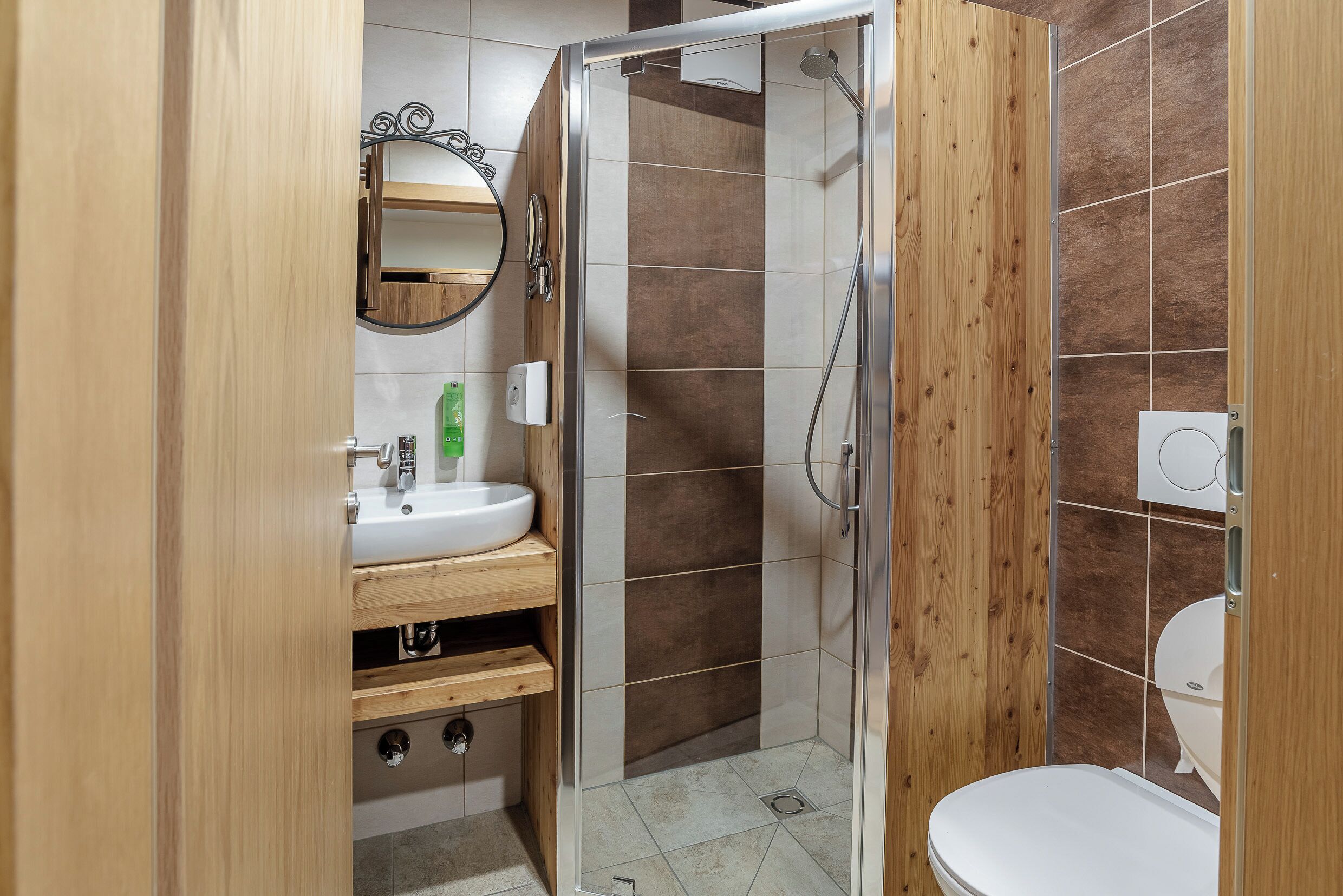 A bathroom with a wooden vanity, a sink, a mirror, a shower enclosure, and a toilet.