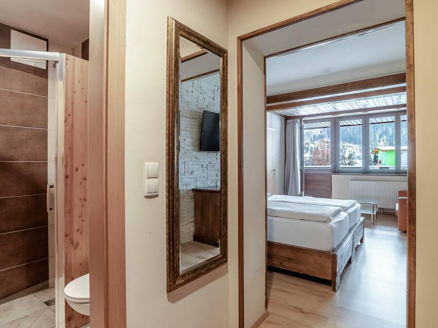 Una habitación con piso de madera, una cama, un ventanal con vistas y un espejo.