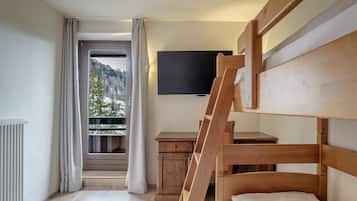 A bunk bed room with a TV, a small wooden desk, and a window with curtains.