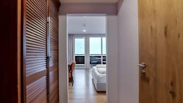 Een hotelkamer met een houten deur, een bed, een bureau en uitzicht op zee door grote ramen.