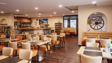 A restaurant with multiple dining tables and chairs, a bar area, and a large wheel mural on the wall.