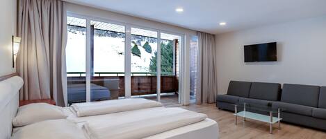 Una sala moderna con un sofá, una mesa de centro de vidrio y una cama con almohadas.