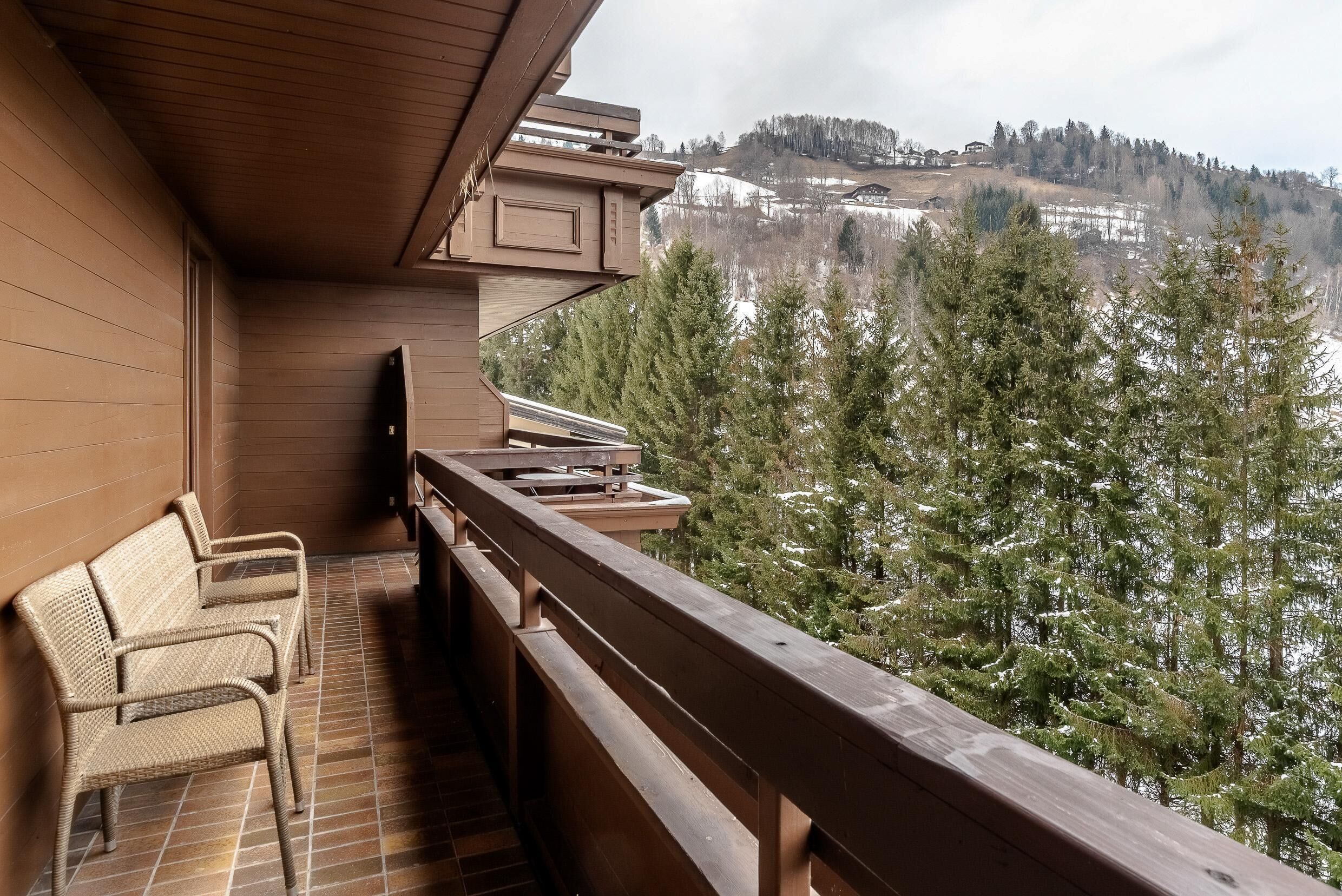 Un balcón con mobiliario de mimbre, barandilla de madera y vista a un paisaje nevado con árboles.