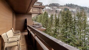 A balcony with wicker furniture, a wooden railing, and a view of a snowy landscape with trees.