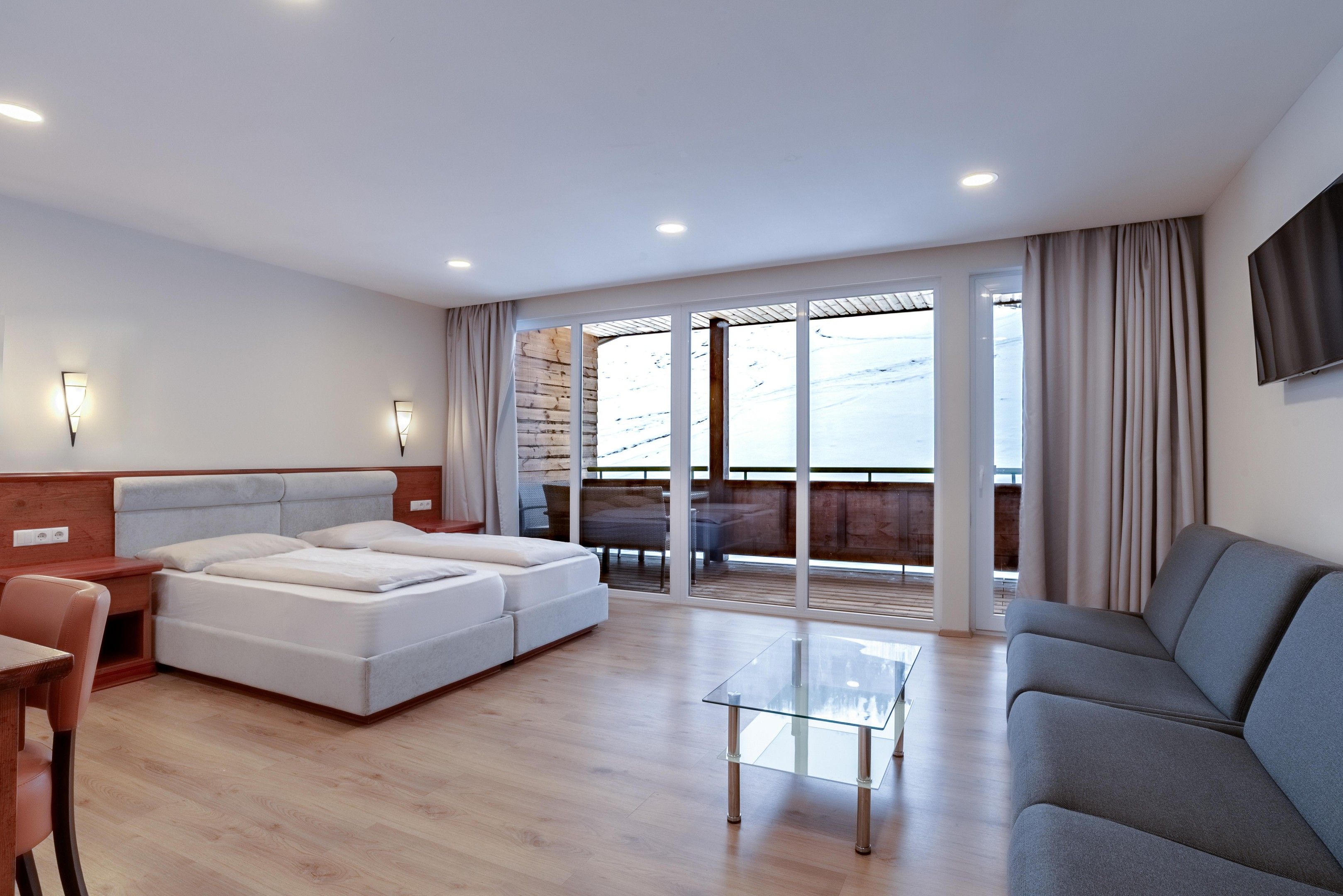 A modern hotel room with a bed, a sofa, a glass coffee table, and a TV.