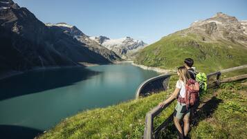 A mountainous landscape with a lake, a wooden bridge, and hikers with backpacks.