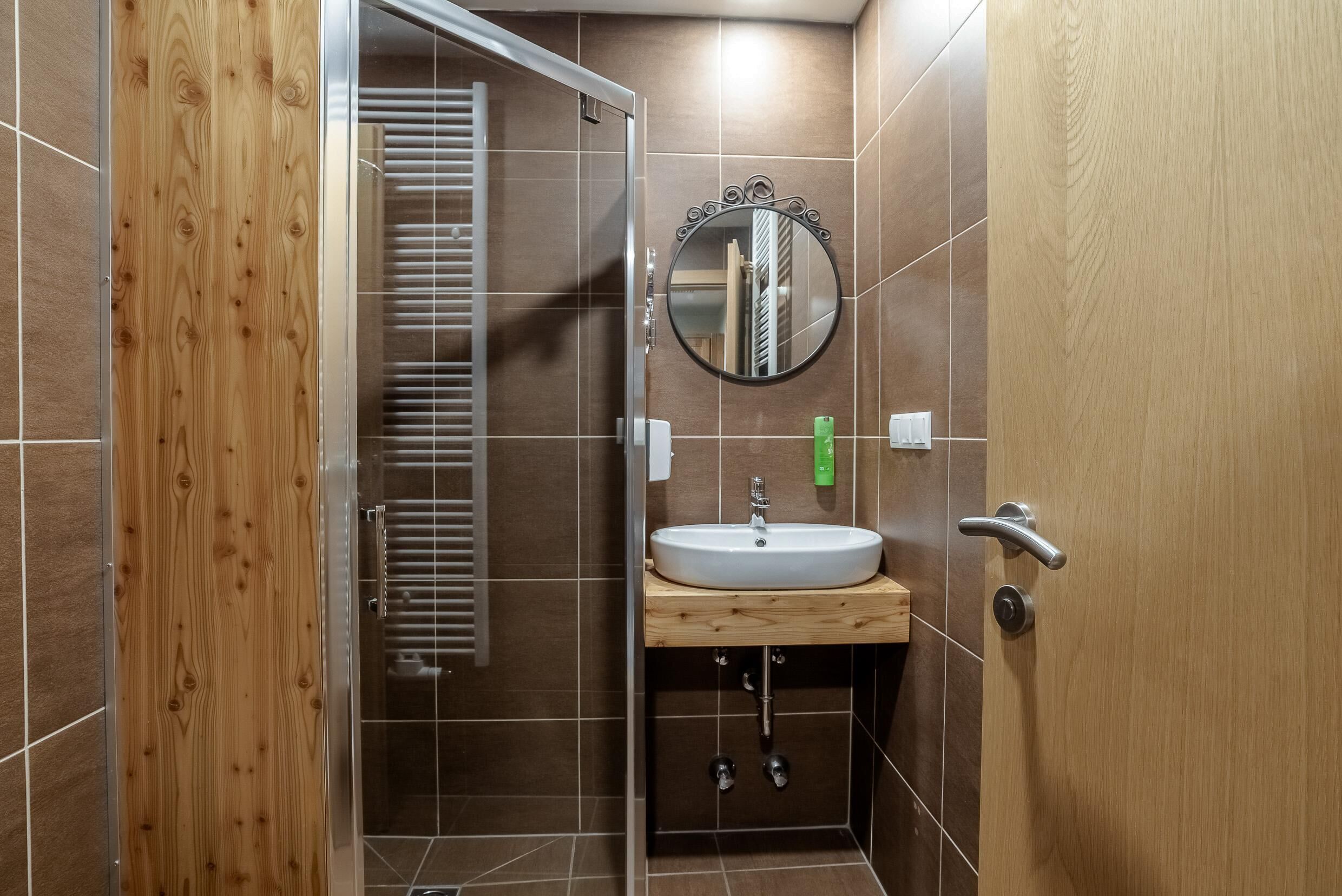 A bathroom with a wooden door, a round mirror, a sink, and a shower area.