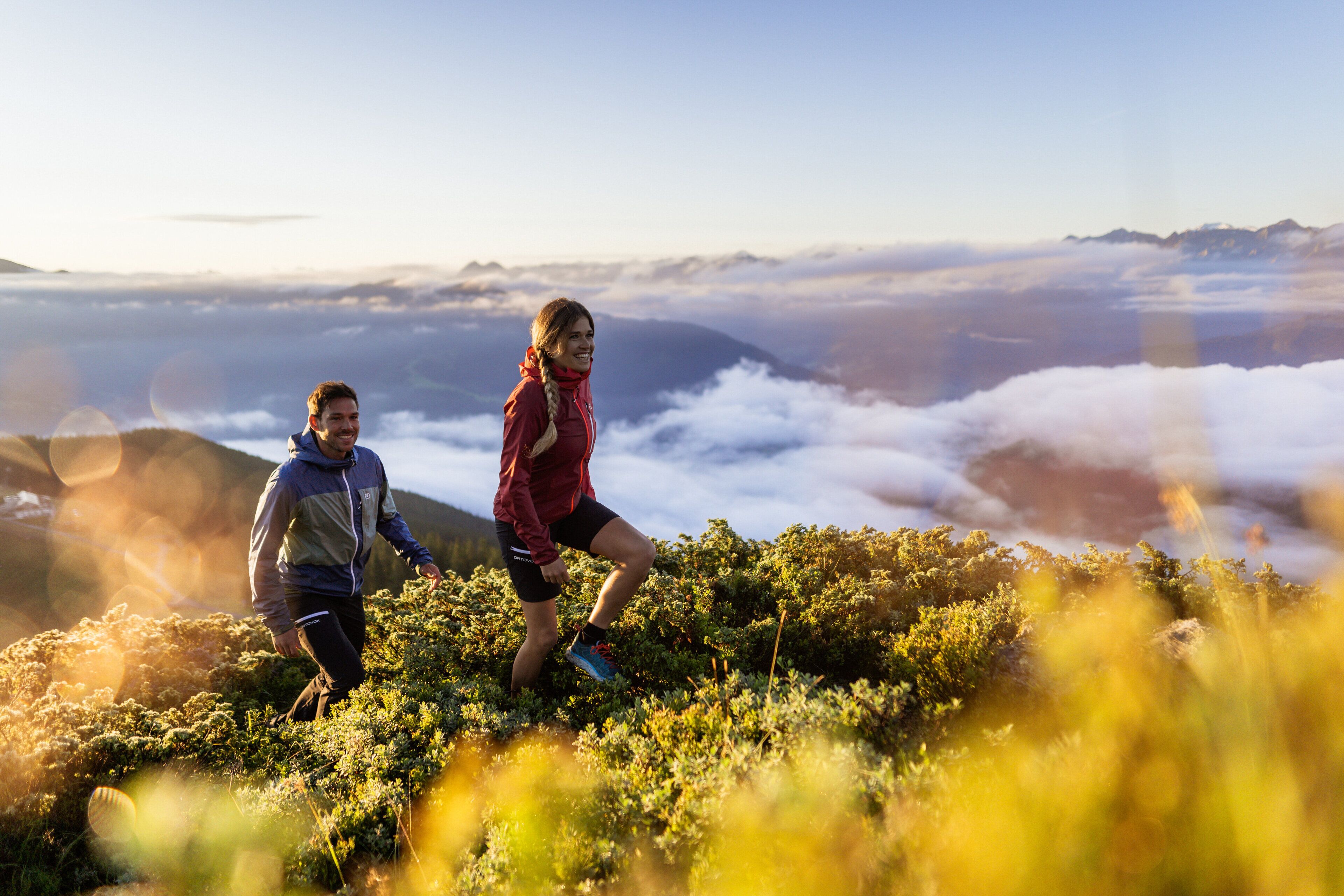 Two people hiking on a mountain with a view of clouds below.