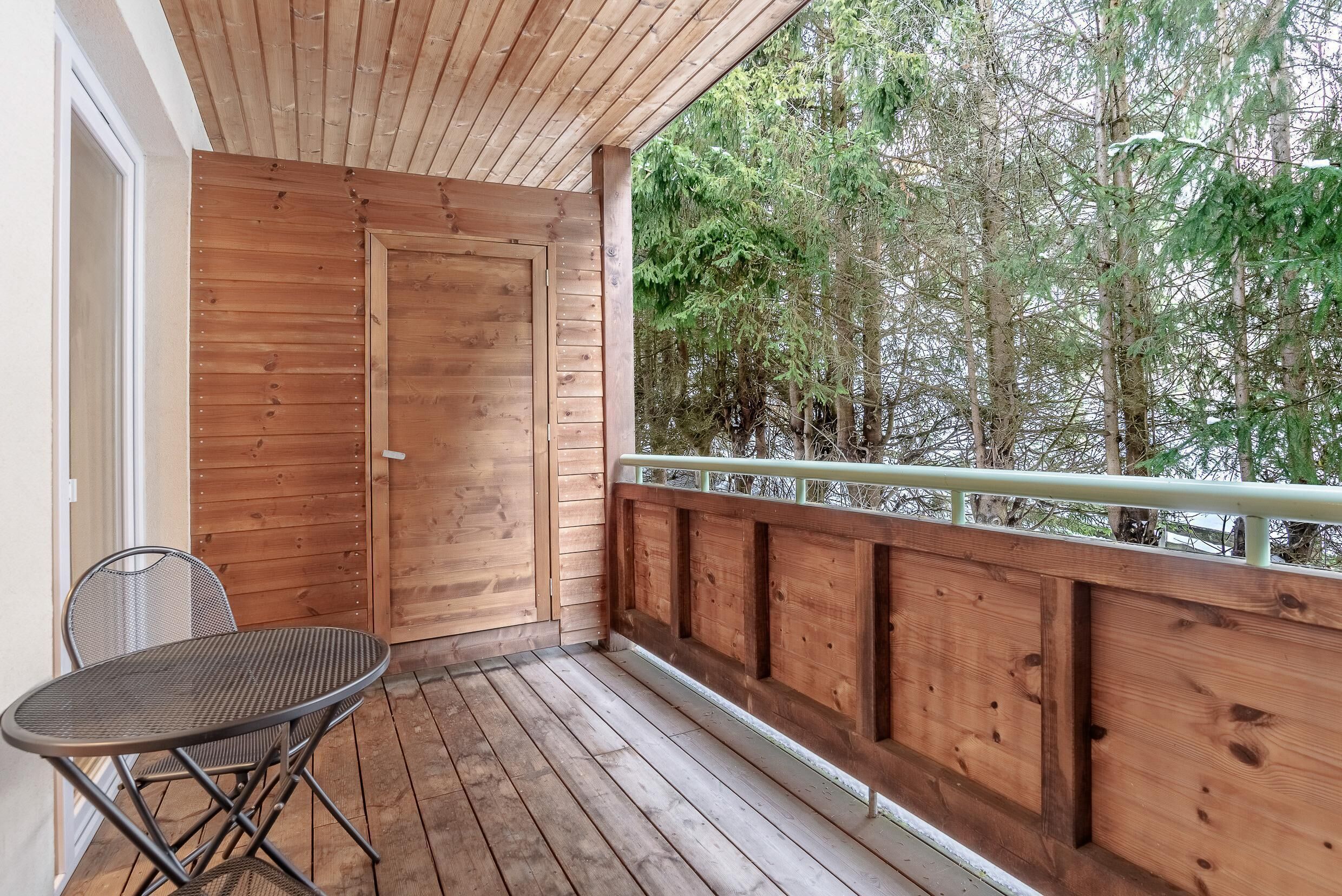 A wooden deck with a metal table and chair, a wooden door, and a view of trees.
