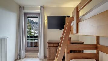 A room with a bunk bed, a flat-screen TV mounted on the wall, a small wooden desk, and a window with curtains.