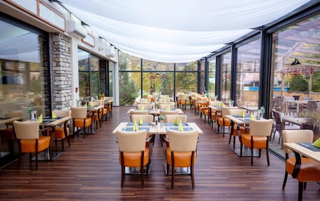 A spacious outdoor dining area with multiple tables and chairs, large windows, and a covered section.