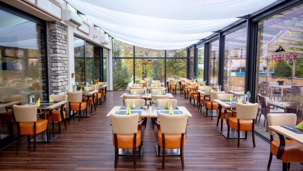A spacious outdoor dining area with multiple tables and chairs, large windows, and a covered section. - Hotel Victoriya (Kaprun)