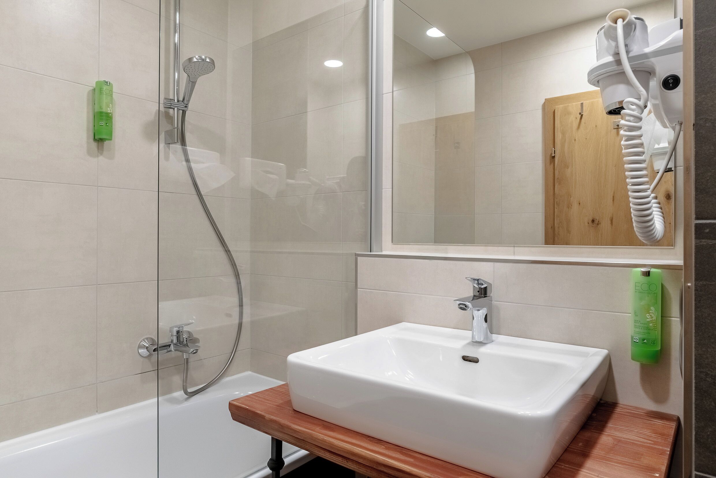 A bathroom with a shower, a sink, a mirror, and a wooden shelf.